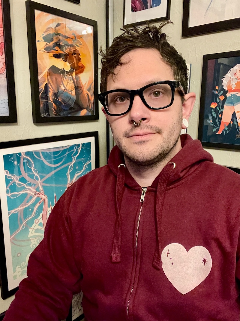 Jo — in glasses and a maroon hoodie, in front of a wall of framed art prints